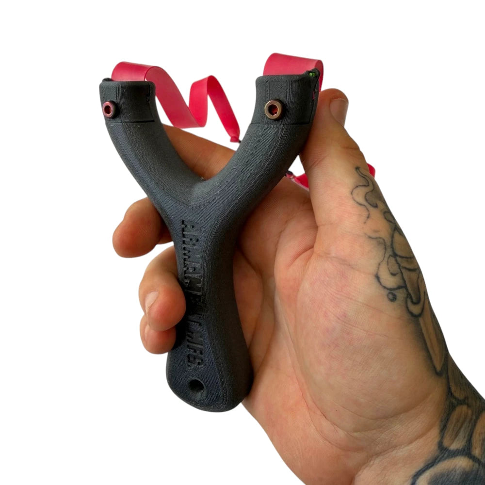 Black slingshot with red band held in a hand against a white background