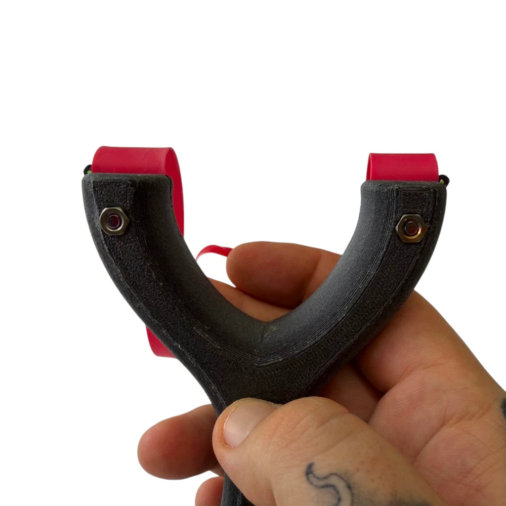 Hand holding a black slingshot with red bands on a white background